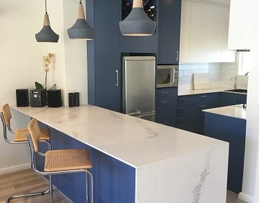 Blue kitchen island with waterfall countertop and integrated breakfast bar.