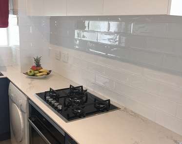 Gas hob installation with quartz countertop and glossy subway tile splashback.