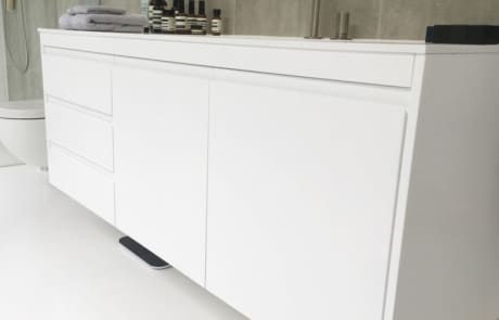 A modern bathroom cabinet with a white finish, featuring multiple drawers and a minimalist design