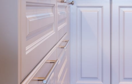 White kitchen cabinets with sleek silver handles, featuring a dark countertop and tiled backsplash.