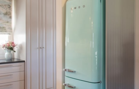 A retro-style mint green refrigerator positioned between cabinetry in a kitchen.