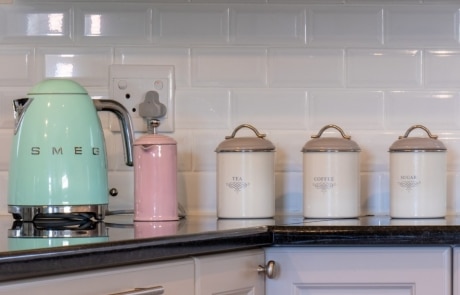 A pastel green kettle and several white canisters lined up on a countertop, with dishes arranged in a cabinet above.