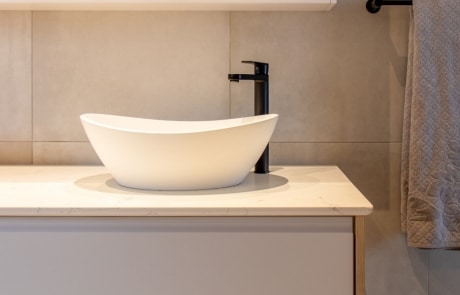 A modern bathroom featuring a sleek white bowl sink on a light countertop, with a faucet and mirrored cabinets above