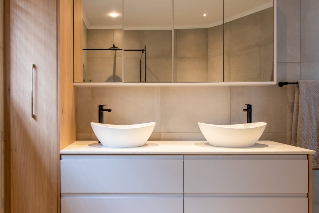 A modern bathroom featuring a double sink vanity with two white bowl sinks, a mirror above, and a minimalist design.
