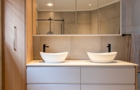 A modern bathroom featuring a double sink vanity with two white bowl sinks, a mirror above, and a minimalist design.