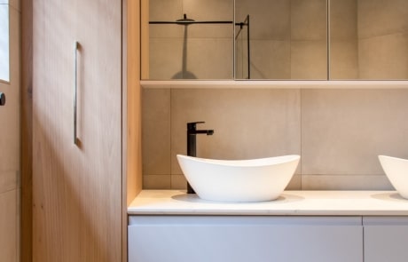 A modern bathroom with a wooden cabinet, a white vessel sink on a countertop, and a large mirrored cabinet above.