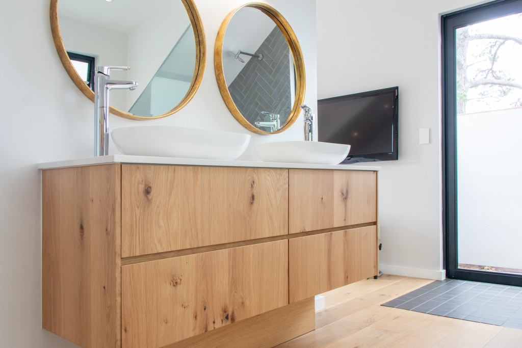 A modern bathroom with a wooden vanity featuring two round mirrors above a sink