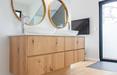 A modern bathroom with a wooden vanity featuring two round mirrors above a sink