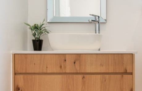 A modern bathroom vanity with a wooden cabinet, a white countertop, a sink, and a mirror on the wall.