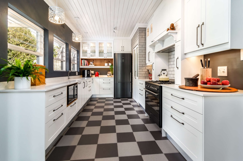 A modern kitchen with white cabinets, a black fridge, and a checkerboard floor.