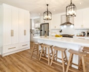 Modern white kitchen with central island seating and pendant lighting above the breakfast counter.