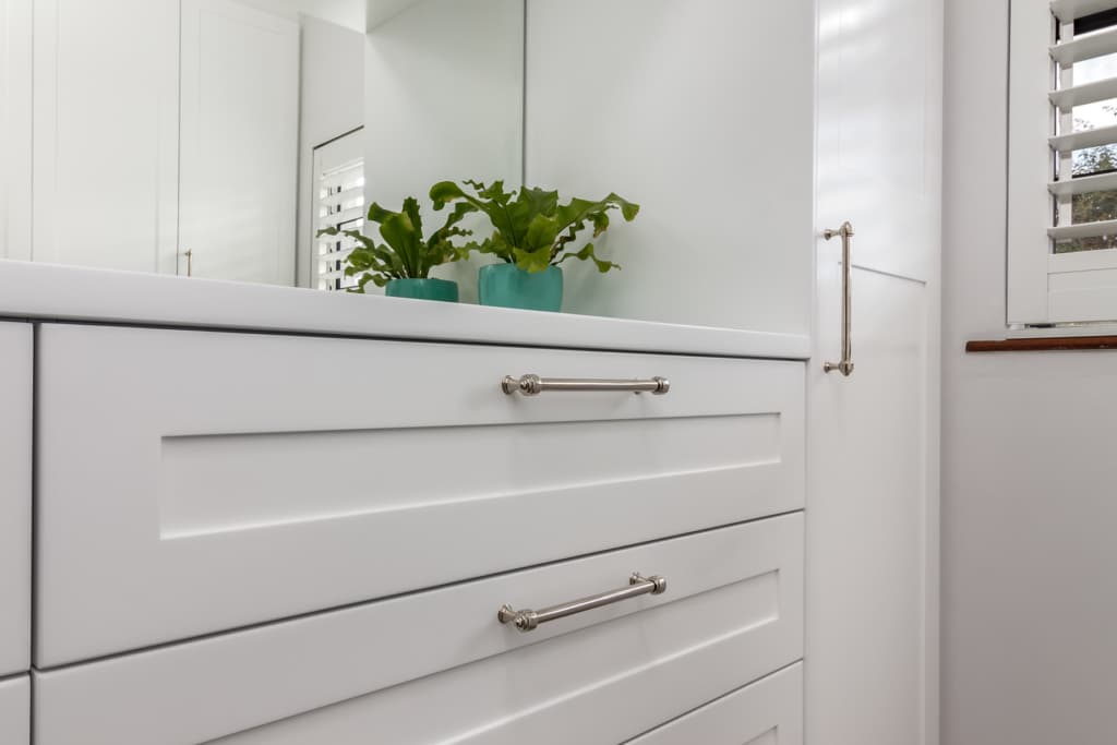 A close-up of a white cabinet with drawers, featuring silver handles and small green plants in teal pots on top