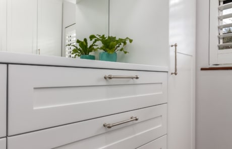 A close-up of a white cabinet with drawers, featuring silver handles and small green plants in teal pots on top