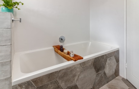 A modern bathroom featuring a white bathtub with a wooden bath caddy, hexagonal tiles on the floor