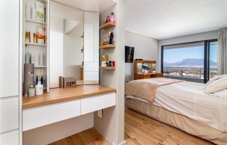 A modern bedroom featuring a large bed, a vanity with a mirror and shelves, and a window with a view of a mountain