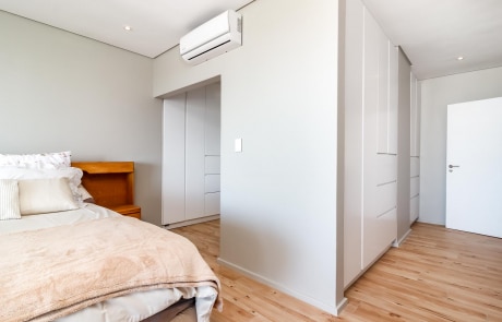 A modern bedroom with a bed, wooden headboard, light wood flooring, and built-in wardrobes.