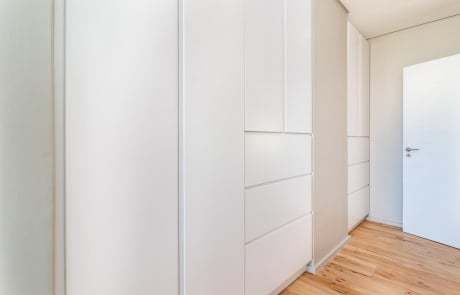 A modern hallway with white cabinetry and wooden flooring, featuring a white door at the end.
