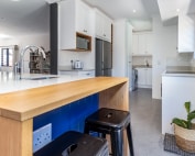 Kitchen breakfast bar with timber countertop, white cabinetry and integrated scullery access.