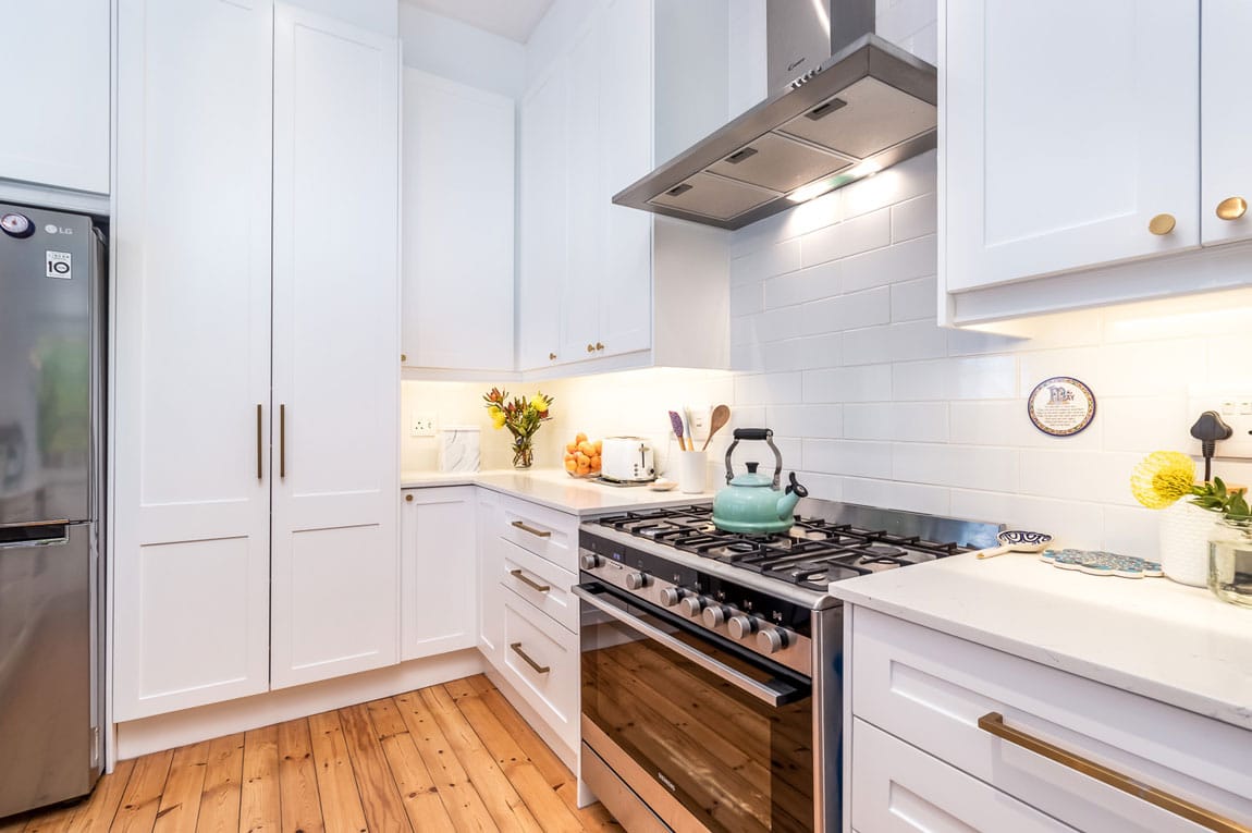 White shaker-style kitchen with gas range, subway tiles, and timber flooring.