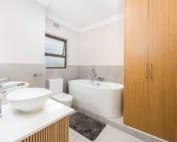 Floor-to-ceiling timber bathroom storage cupboard beside freestanding bath.