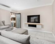A modern living room with a light-colored sofa, an armchair, and a flat-screen TV mounted on the wall