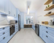 Light blue shaker kitchen with floating timber shelves and wine rack